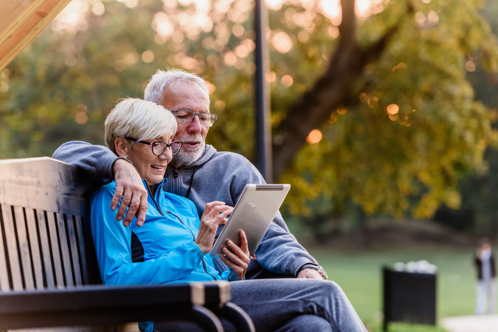 Elderly couple sitting on bench using IPad