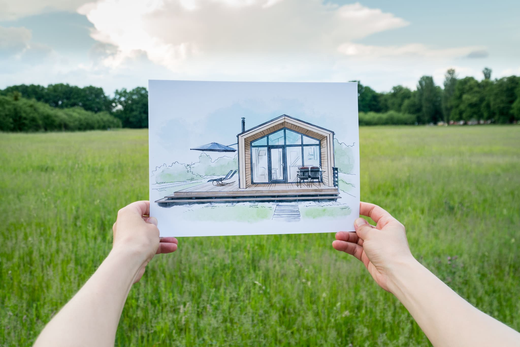 Person in a field holding a drawing of a house